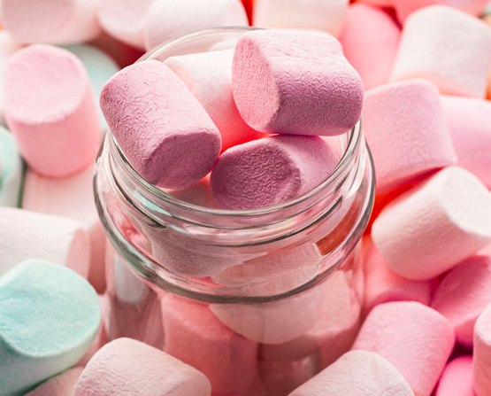 Visual composition of a jar filled to the brim with marshmallows and surrounded by marshmallows